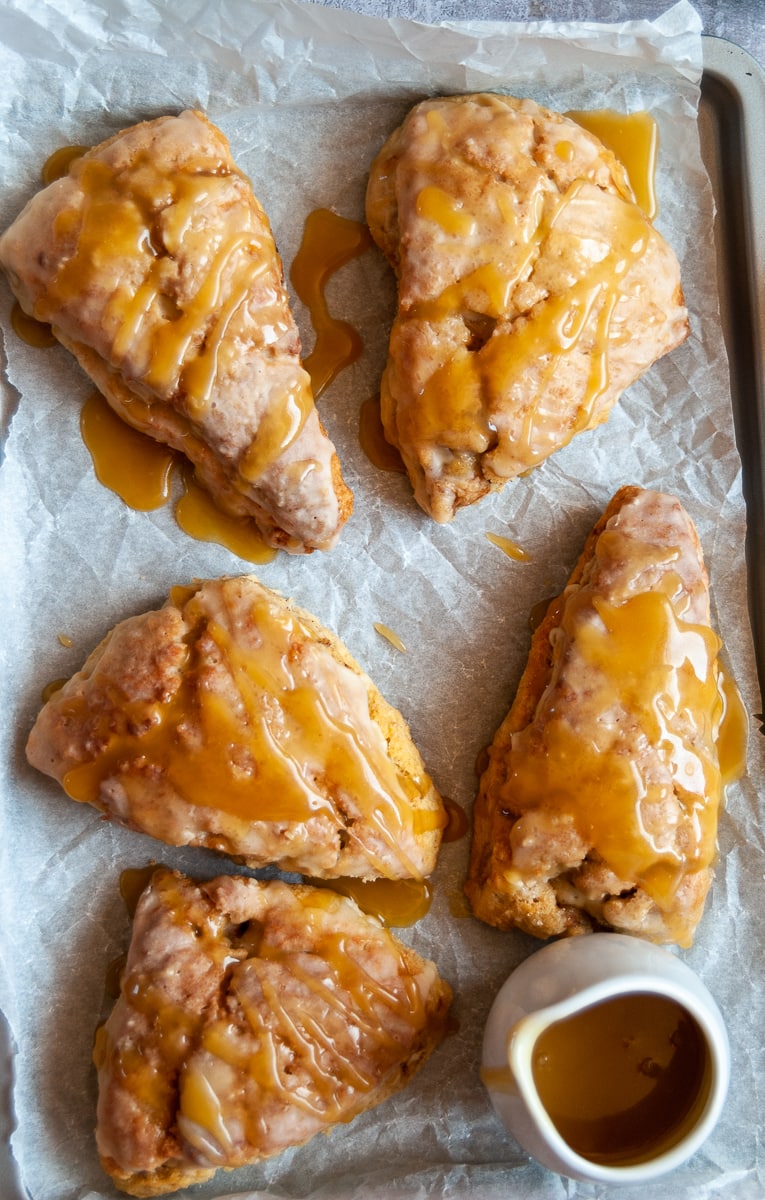 five apple and cinnamon scones with a salted caramel glaze on a baking tray with a small jug of caramel glaze