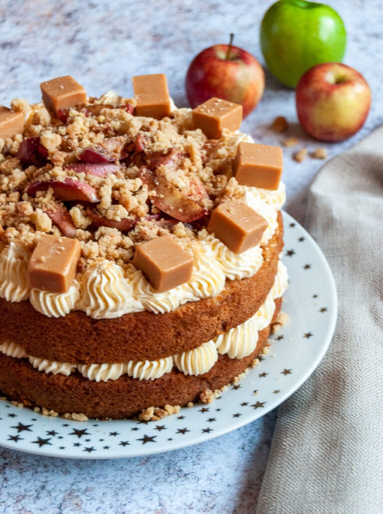 An Apple Cake on a white and gold star plate decorated with custard buttercream, caramelised apples and fudge chunks