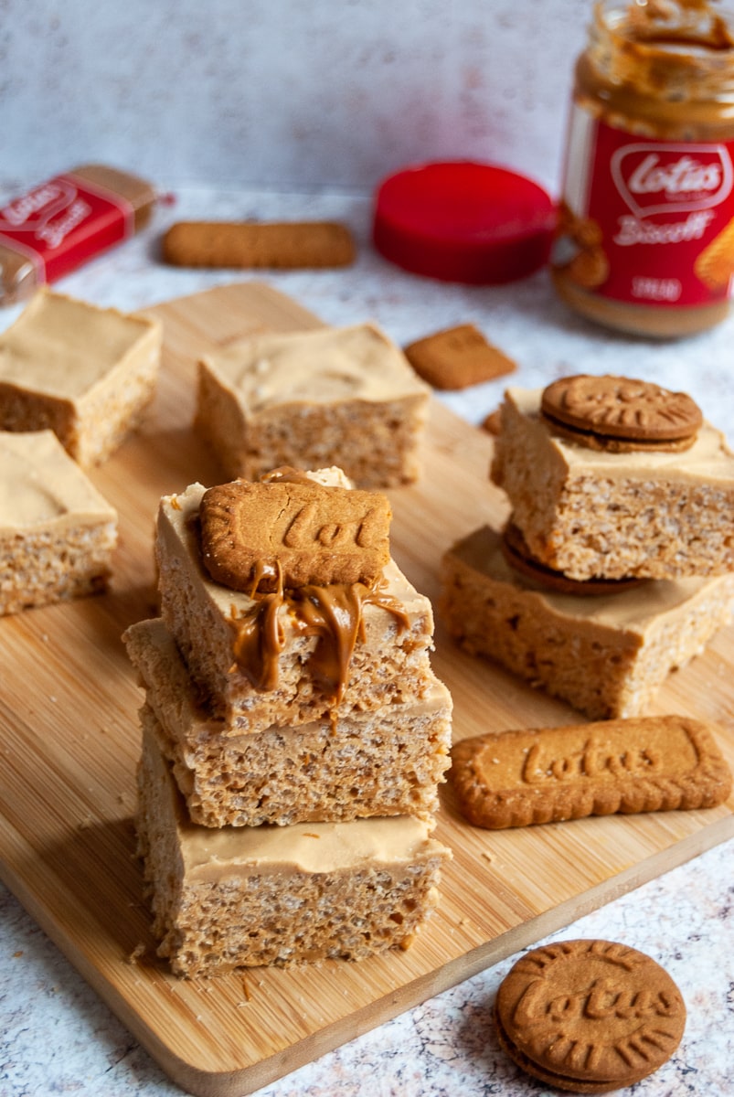 squares of biscoff marshmallow krispies on a wooden board, biscoff cookies and a jar of biscoff spread in the background