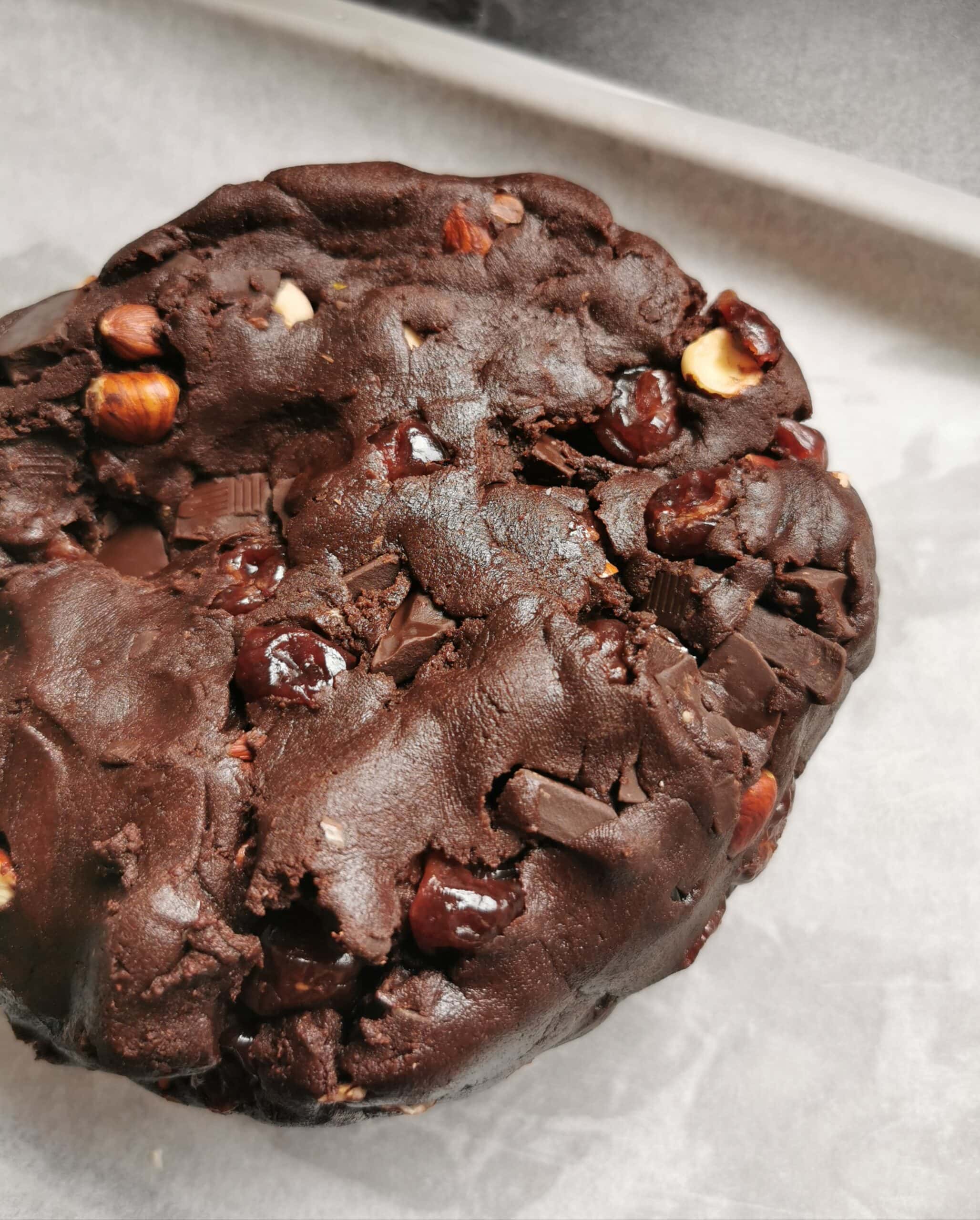 An unbaked chocolate biscotti dough with dried cherries nuts and chocolate chunks on a parchment lined baking sheet