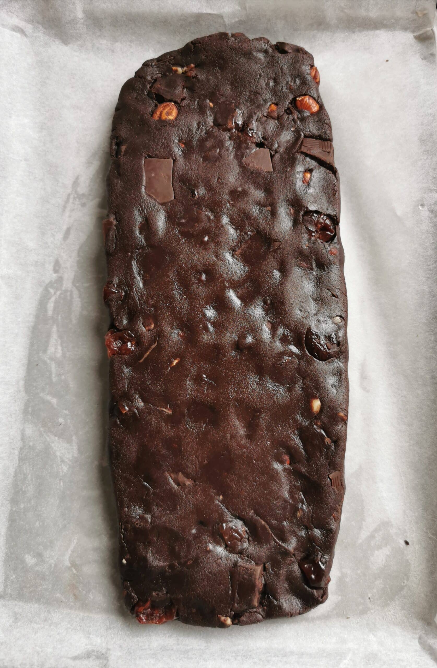 A chocolate biscotti dough shaped into a rectangle on a parchment lined baking sheet