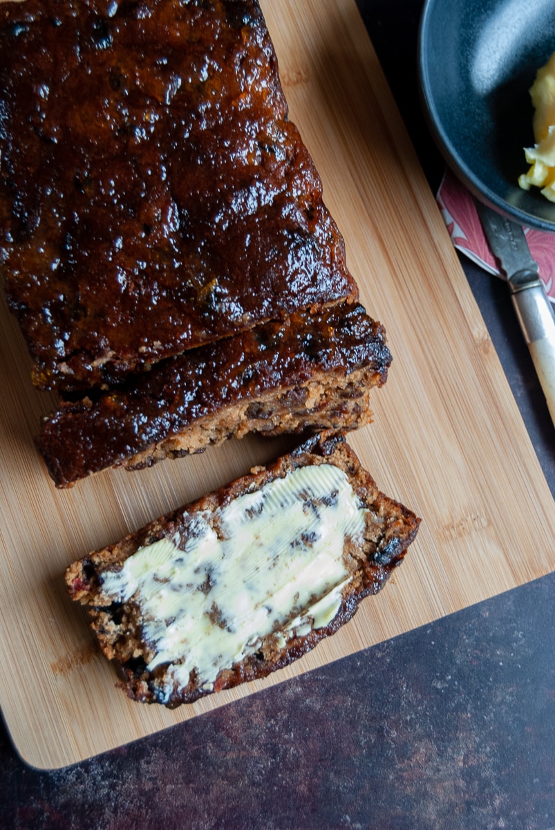 a fruit Barmbrack on a wooden board. A slice has been spread with butter