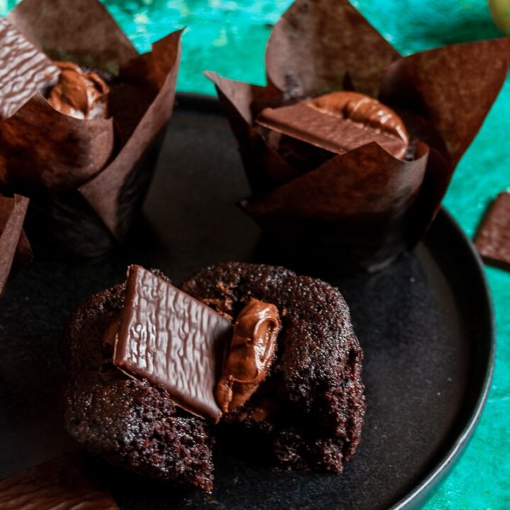 chocolate muffins topped with chocolate ganache and an after eight chocolate on a black plate/green background