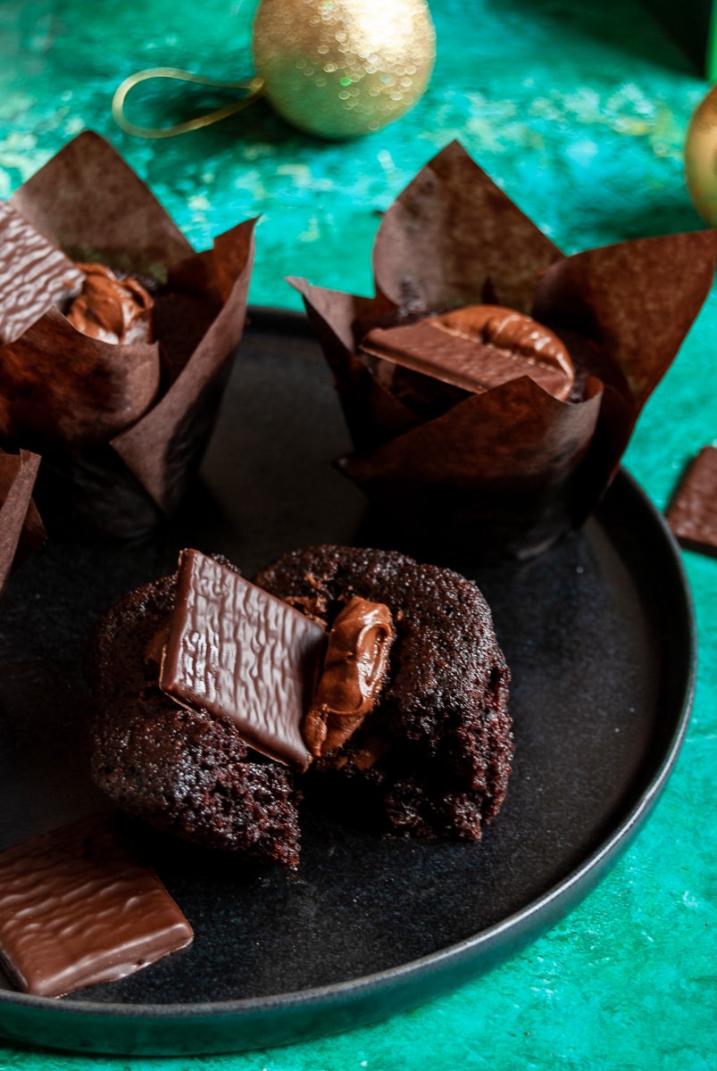 chocolate muffins topped with chocolate ganache and an after eight chocolate on a black plate/green background