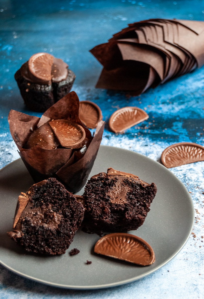 a chocolate orange muffin on a grey plate cut in half to reveal a chocolate ganache middle.