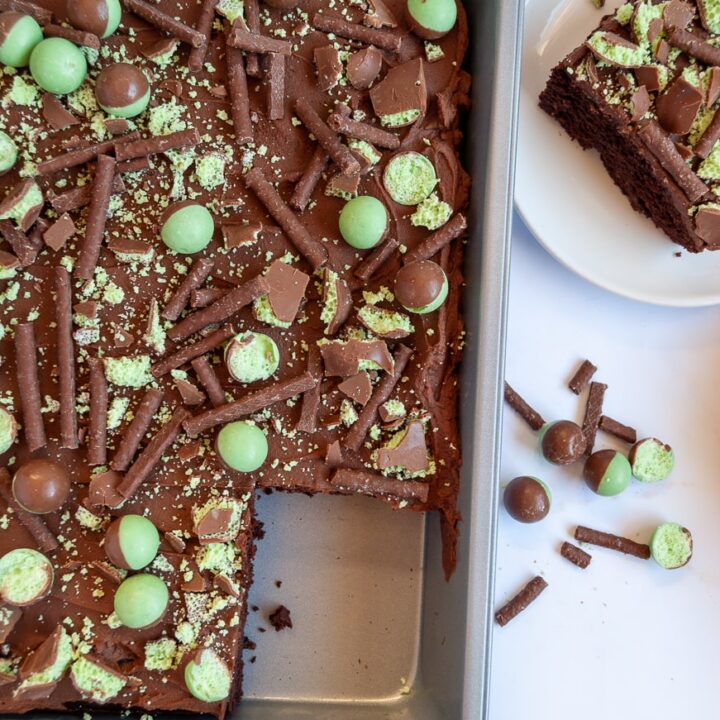 A chocolate sheet cake covered with chocolate ganache and topped with mint aero bubbles in a silver baking pan and a white plate with a piece of chocolate cake