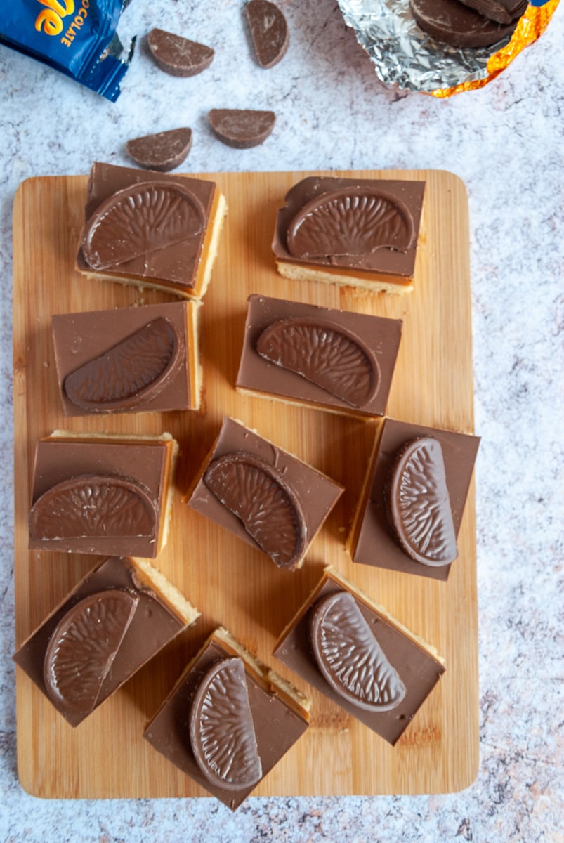 squares of chocolate caramel shortbread topped with a terrys chocolate orange segment on a wooden board