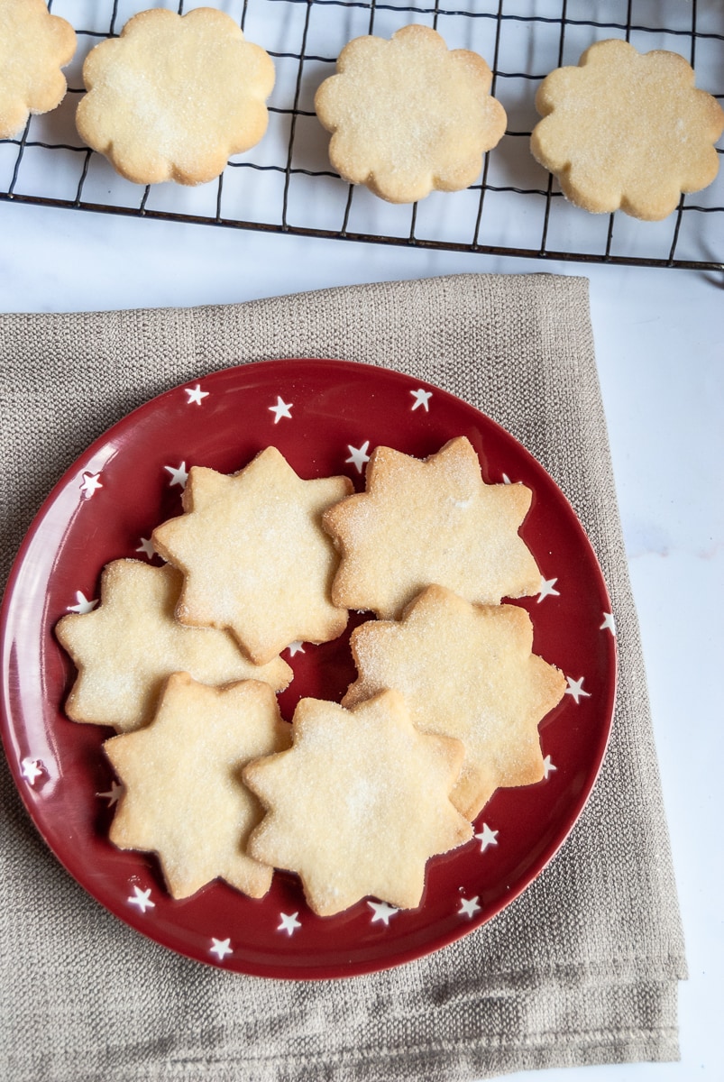 shortbread stars on a red and white star plate, a beige napkin and a wire cooling rack with more shortbread