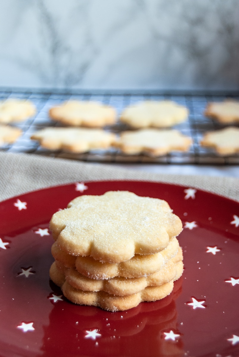 round Shortbread biscuits on a red and white star plate. More shortbread on a wire cooling rack can be seen in the background