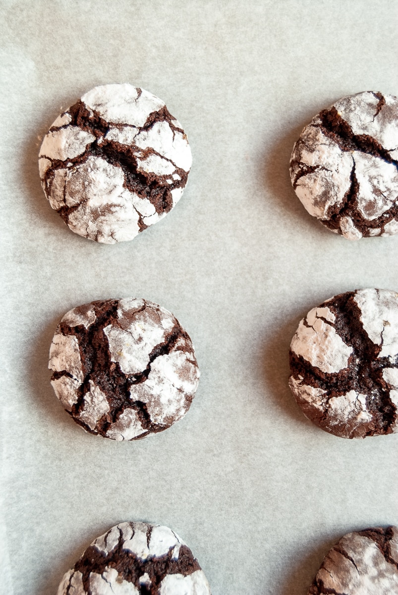 a close up photo of chocolate cookies dusted with icing sugar on a silver baking sheet