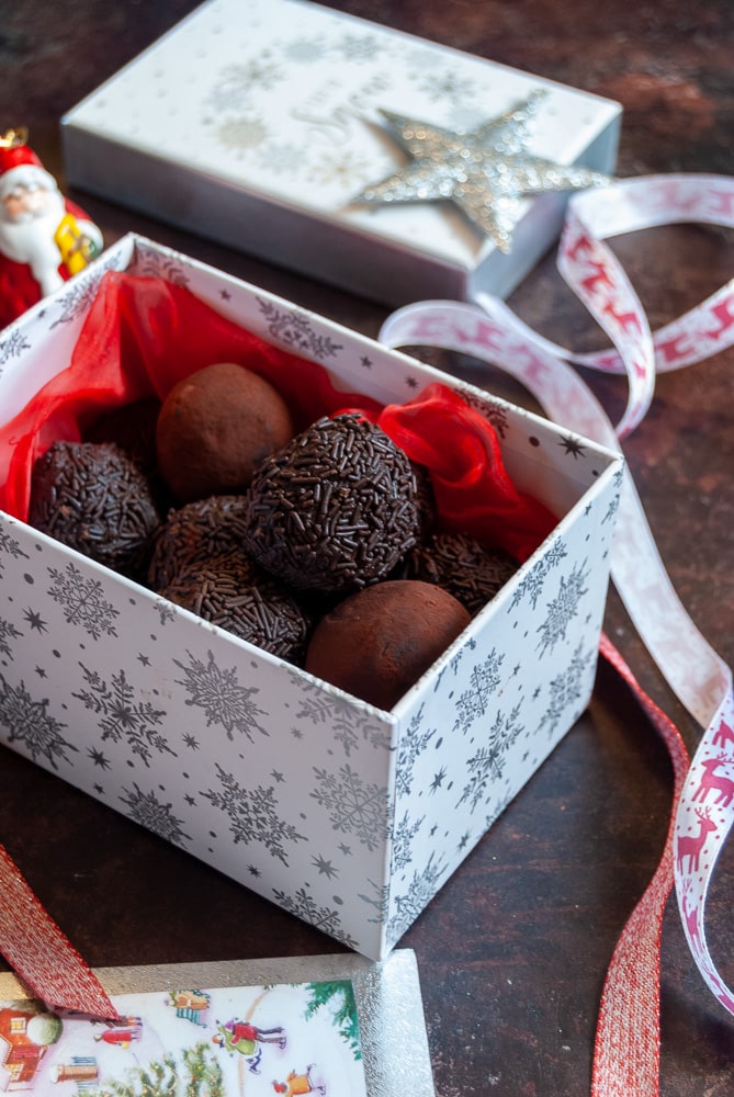 a white and silver snowflake gift box filled with red tissue paper and chocolate rum truffles, red and white Christmas ribbon and a santa figure