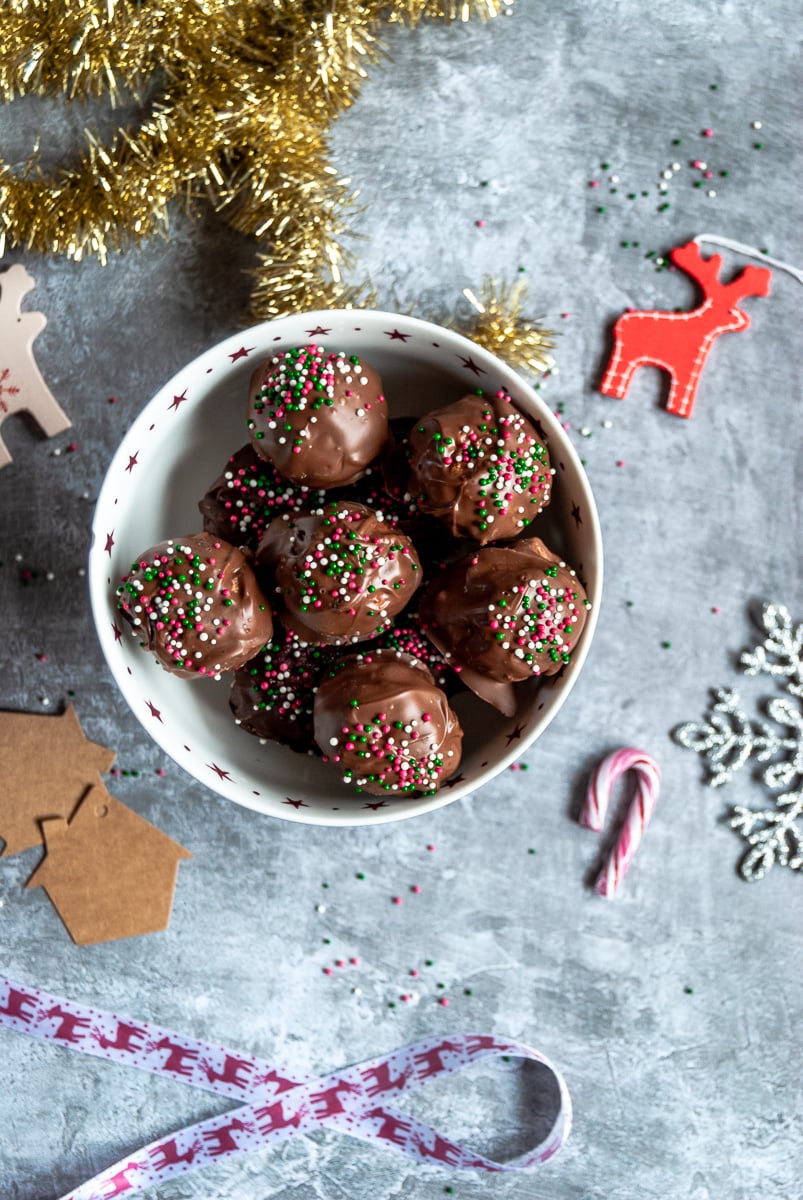 a red and white star bowl filled with chocolate peanut butter balls covered in Christmas sprinkles, red and white ribbon with reindeers, gold tinsel and red and white reindeer decorations and gold tinsel