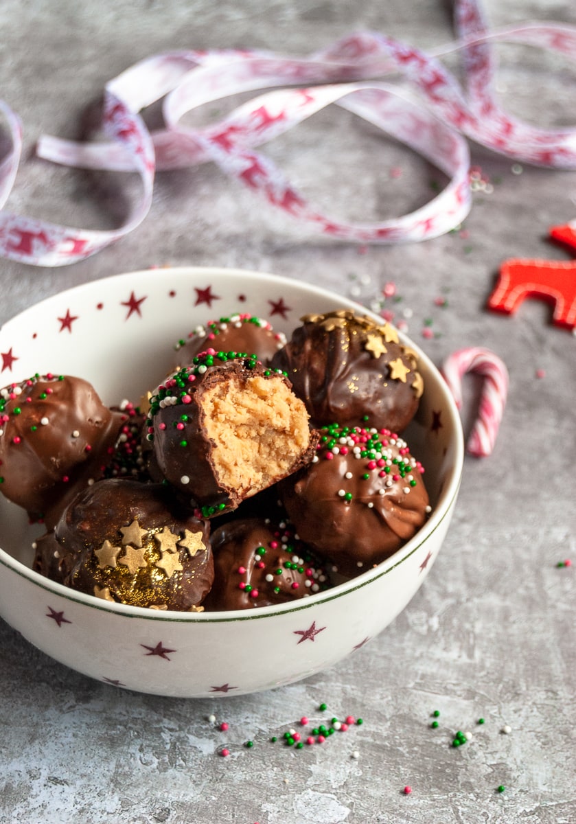 a red and white star bowl filled with chocolate peanut butter truffles covered in Christmas sprinkles. Red and white ribbon in the background