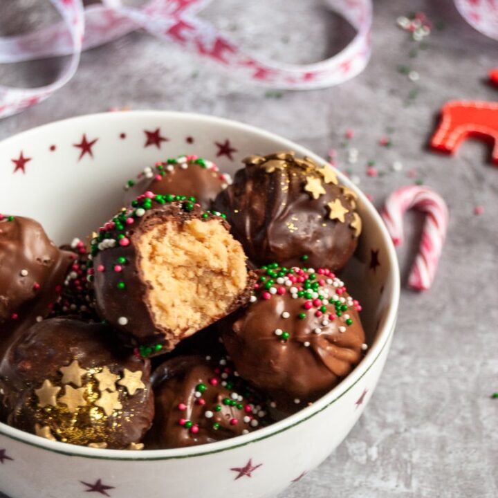 a red and white star bowl filled with chocolate peanut butter truffles covered in Christmas sprinkles. Red and white ribbon in the background