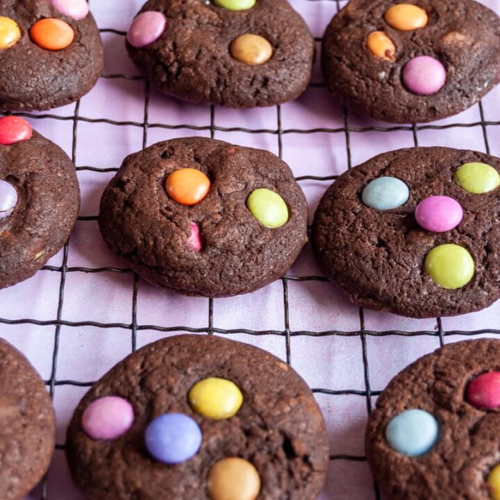 a batch of chocolate cookies topped with smarties on a black wire rack.