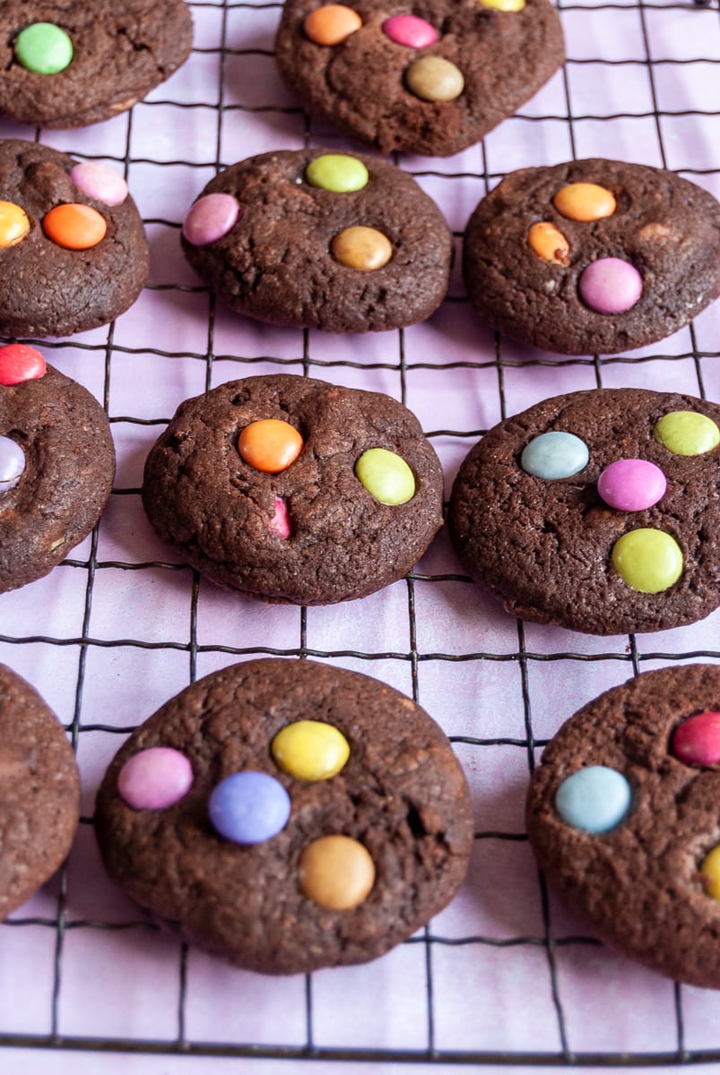 a batch of chocolate cookies topped with smarties on a black wire rack.