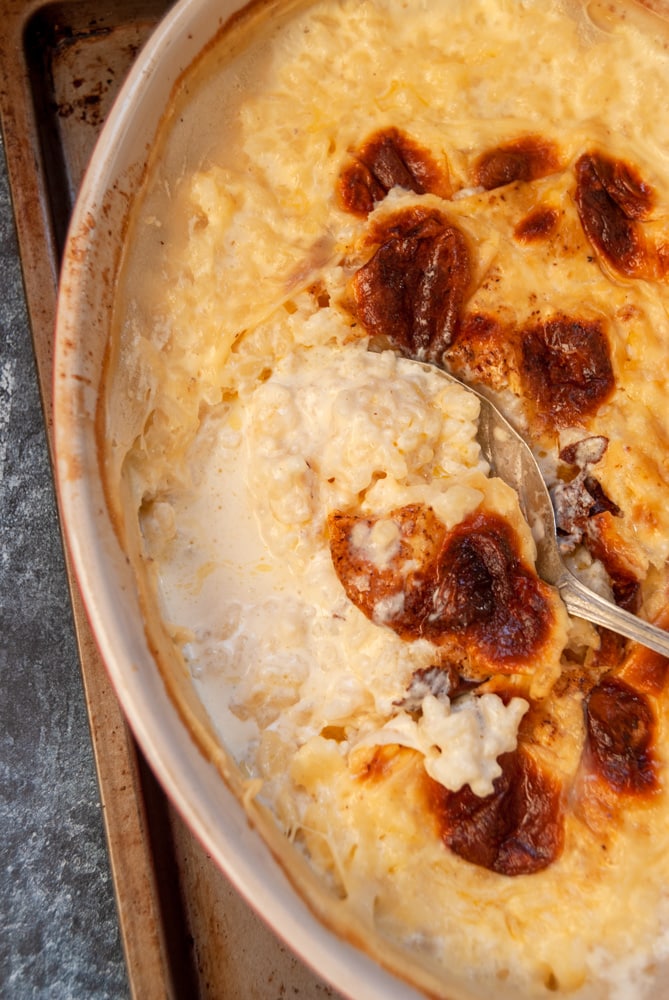 A close up photo of a dish of baked rice pudding with a silver serving spoon.