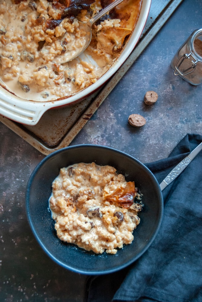 A black bowl of rice pudding with sultanas and a black napkin with a silver spoon.