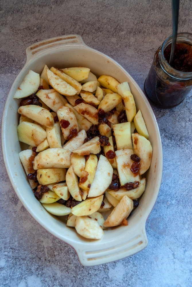 sliced apples and mincemeat in an oval dish and a jar of mincemeat with a spoon on a grey worktop