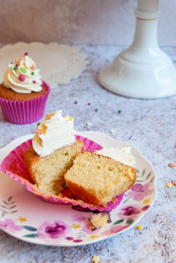 a vanilla cupcake topped with vanilla buttercream cut in half on a floral plate.