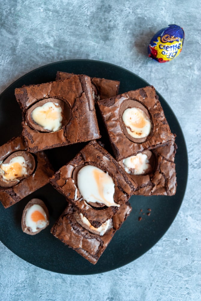 chocolate brownies topped with creme eggs on a black plate and grey background.