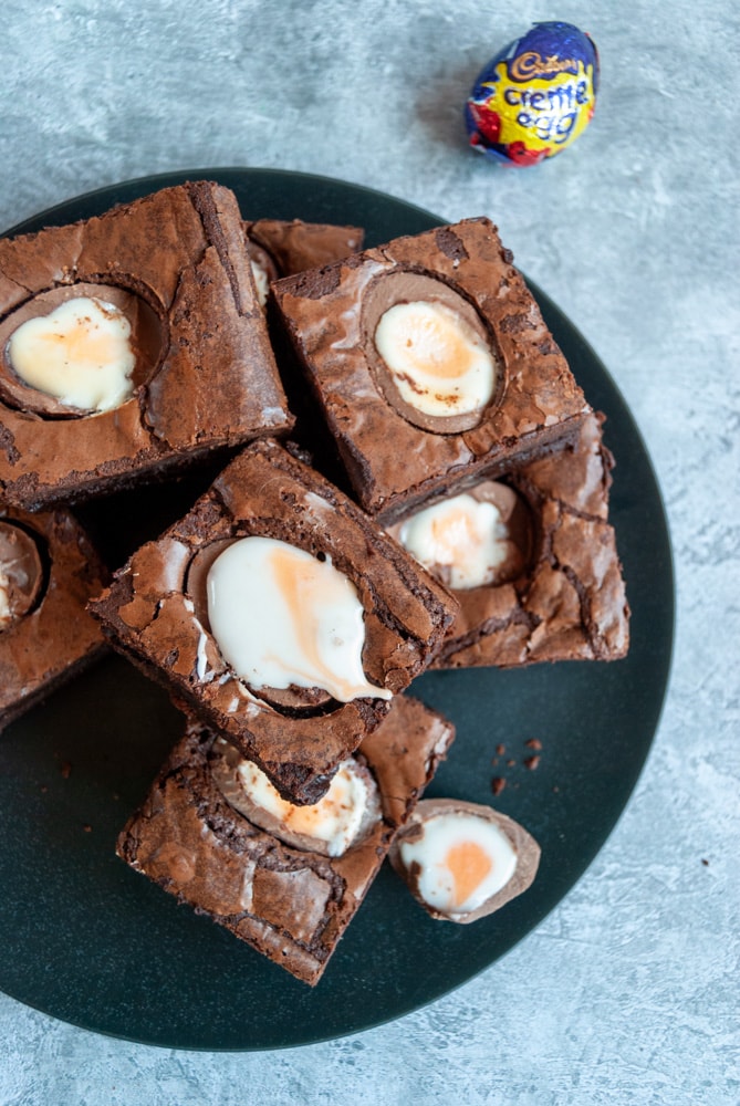 a flat lay photo of a black plate of chocolate brownies topped with creme eggs.