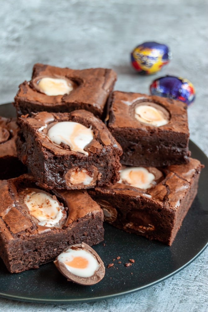 a black plate of chocolate brownies topped with creme eggs.  