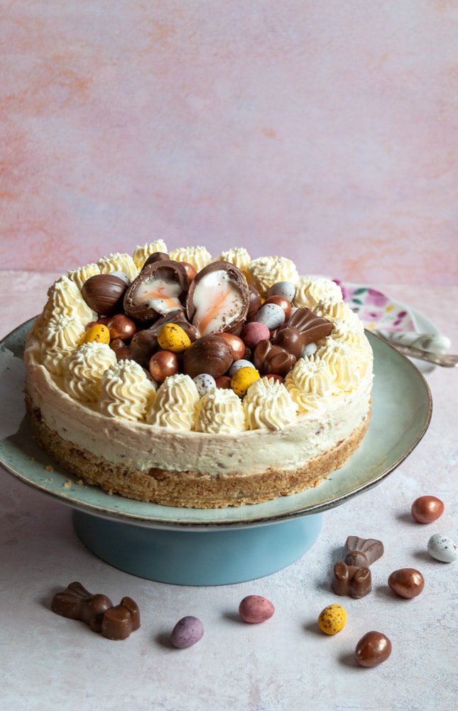 a large cheesecake decorated with whipped cream swirls and Easter chocolate on a blue plate.