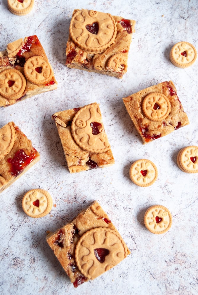 a flat lay image of jammie dodger blondies and mini jammie dodger biscuits on a light grey background.