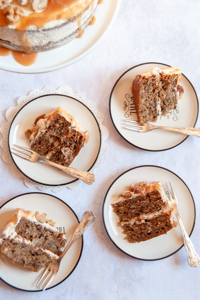 Four small plates with a slice of banana cake with caramel buttercream and a silver cake fork on each one.