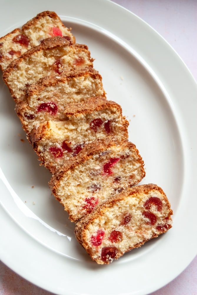 Slices of a cherry and coconut loaf cake on a white oval dish.