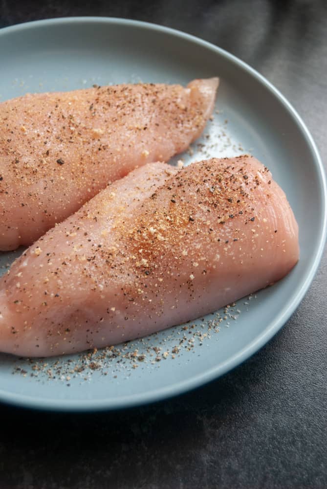 two seasoned chicken breast fillets sitting on a blue plate.