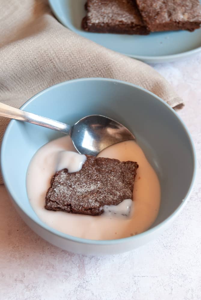 a blue bowl with a chocolate slice, pink custard and a silver spoon with a grey napkin.