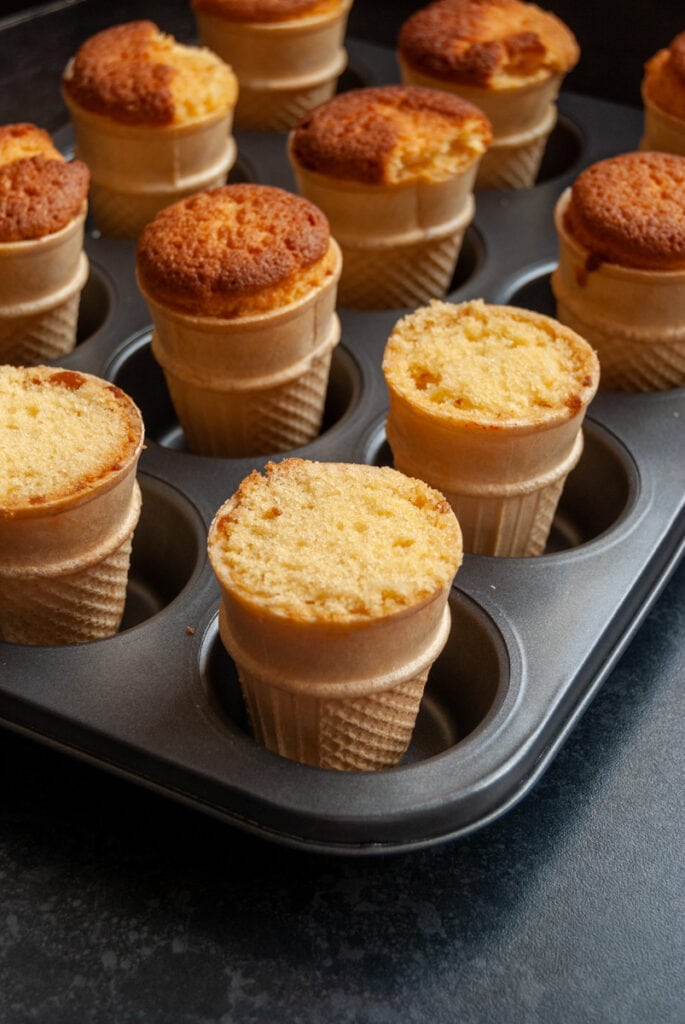 a muffin tin with 12 freshly baked ice cream cones filled with vanilla sponge.
