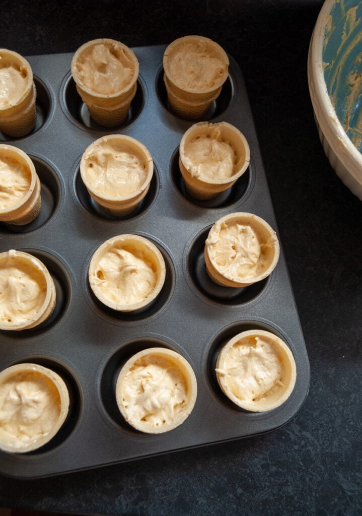 a muffin tin with 12 ice cream cones filled with vanilla cupcake batter.