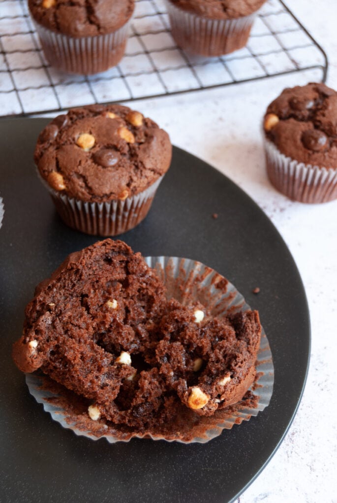 a chocolate muffin broken in half on a black plate