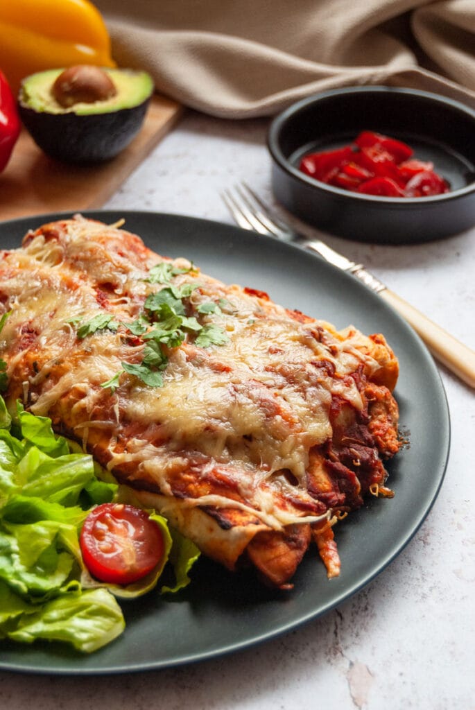 a black plate with two chicken enchiladas, lettuce and tomatoes.