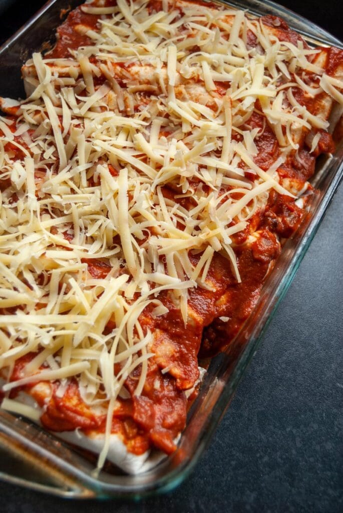 chicken enchiladas sprinkled with grated cheese in a pyrex dish.