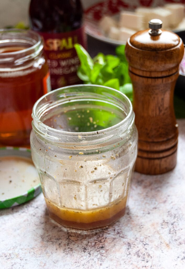a jam jar of salad dressing, a pepper mill, a pot of honey and fresh herbs.