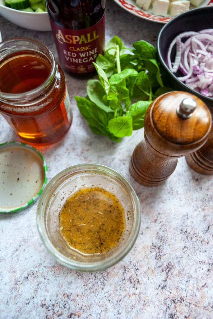 a jam jar of salad dressing, a pepper mill, a pot of honey and fresh mint and basil.