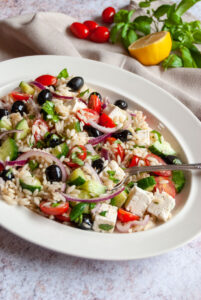 a Greek pasta salad with Orzo on a white oval plate.