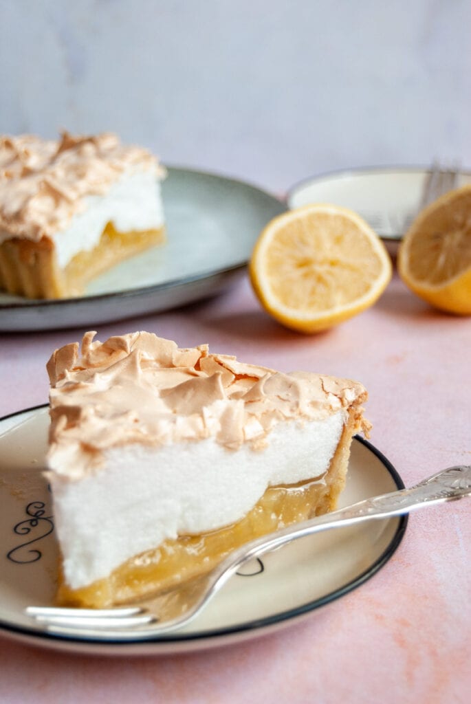 a slice of lemon meringue pie with a silver fork on a white plate