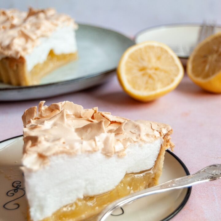 a slice of lemon meringue pie with a silver fork on a white plate