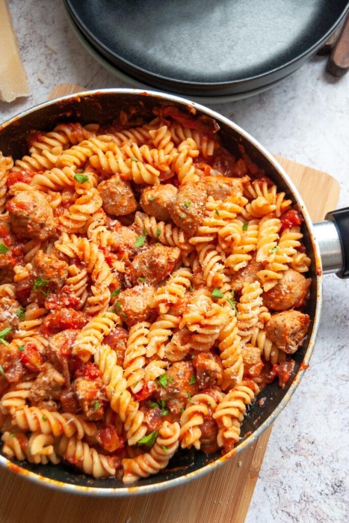 a saucepan of pasta twists and a sausage tomato sauce.