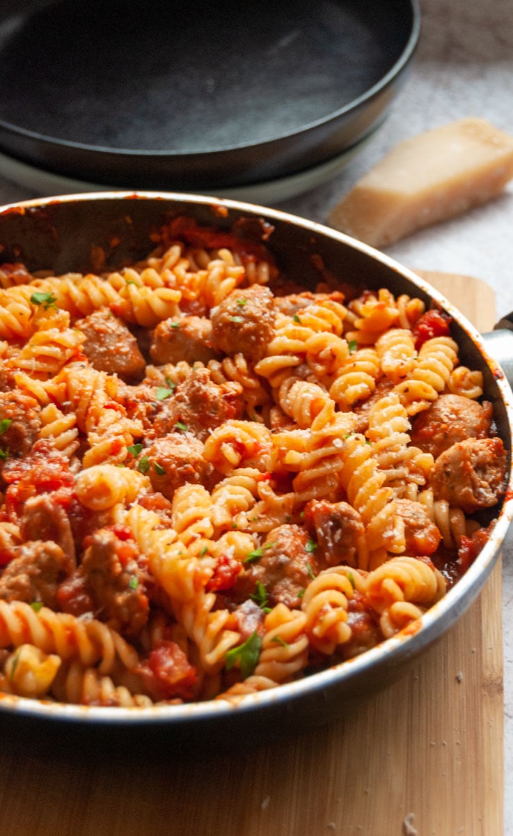 a large saucepan of pasta twists and a sausage tomato sauce.