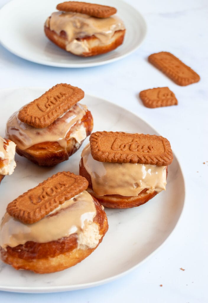 a plate of four doughnuts filled with Biscoff cream and topped with a Biscoff glaze and a Lotus cookie.