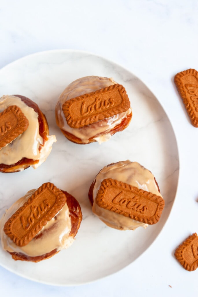 four doughnuts topped with Biscoff glaze and a Lotus Biscoff cookie on a white plate.