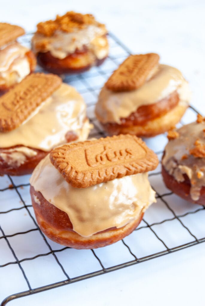 six doughnuts topped with Biscoff glaze and a Biscoff cookie on a wire cooling rack.