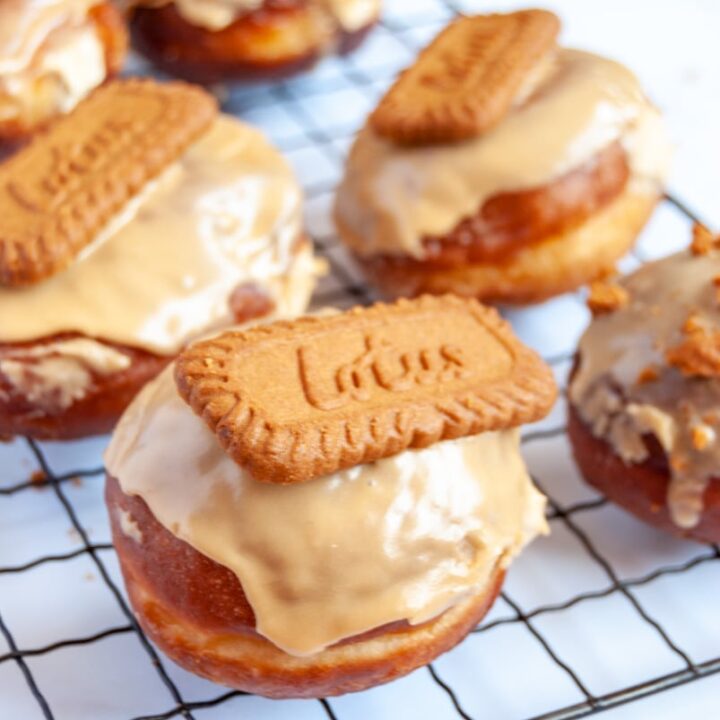 six doughnuts topped with Biscoff glaze and a Biscoff cookie on a wire cooling rack.