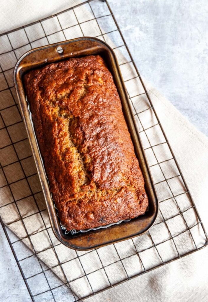 a banana loaf cake in a loaf pan on a black wire rack